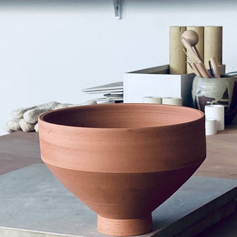 Taça de grés sobre uma base, com peças em prateleiras ao fundo